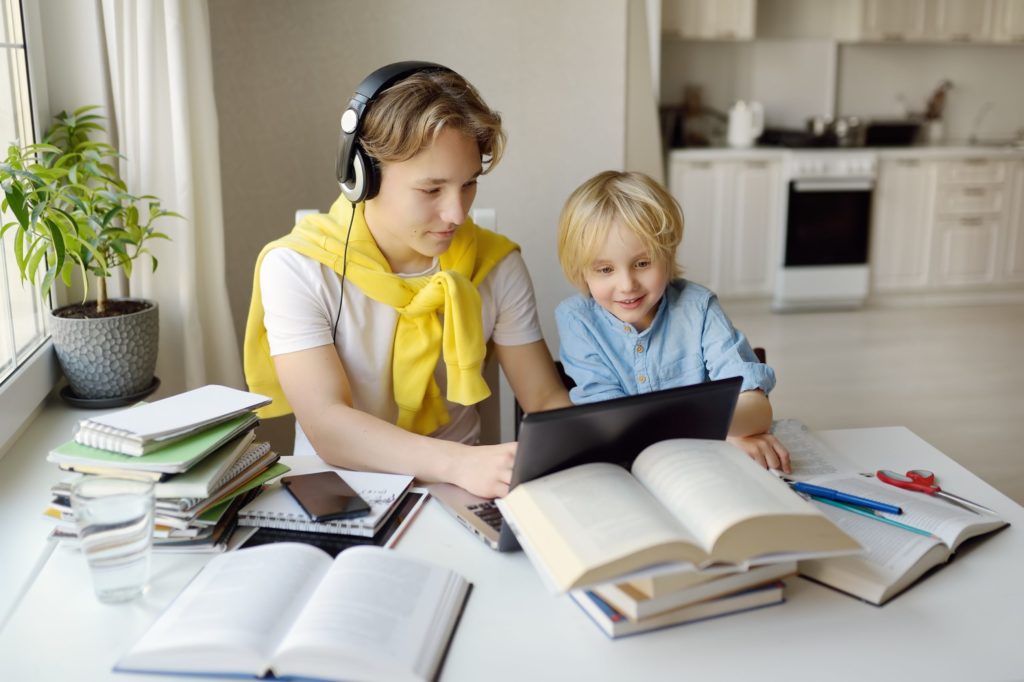 Teenager boy study at home. His younger brother is playing near. Online education and distance learn